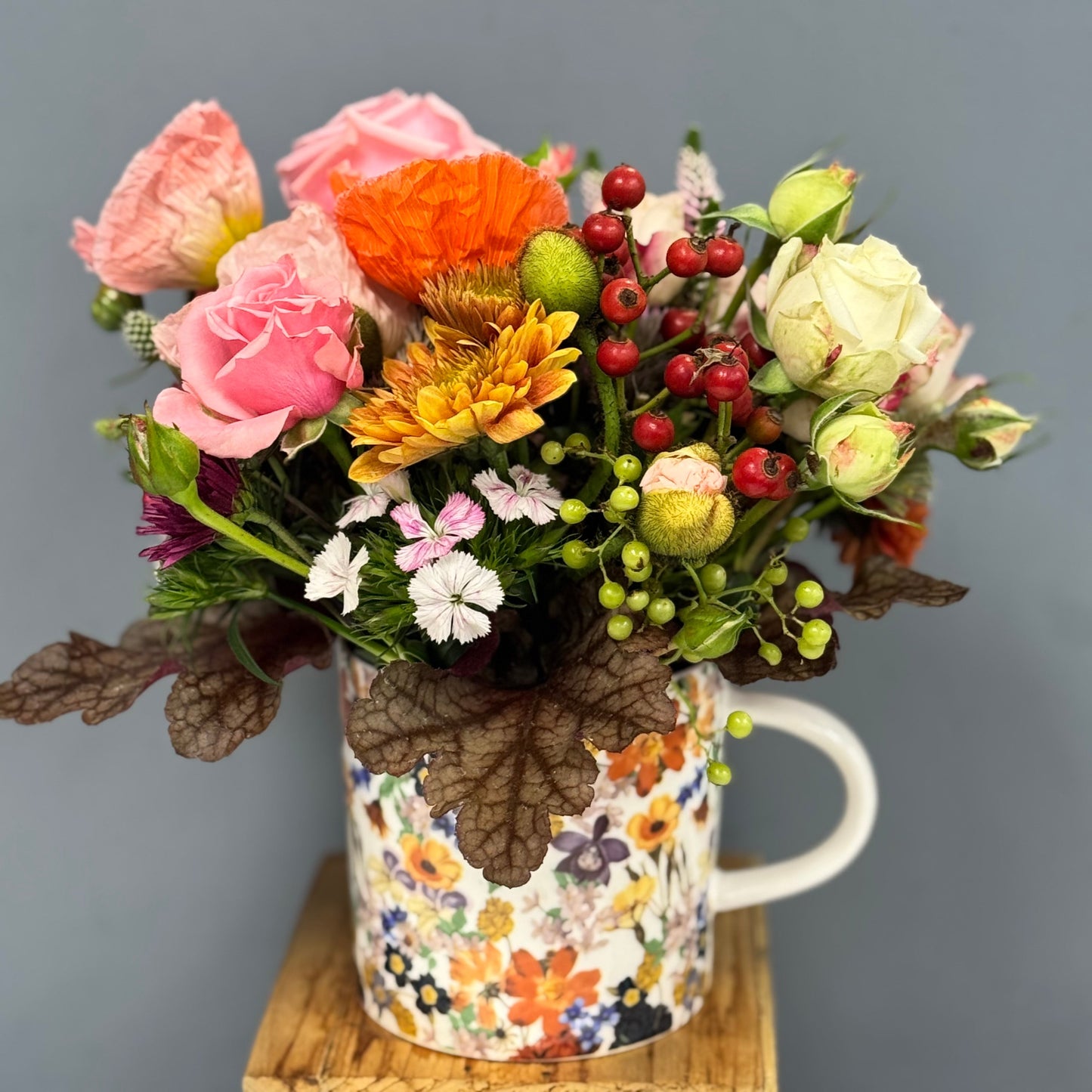Colorful bouquet of flowers in a decorative mug against a gray background